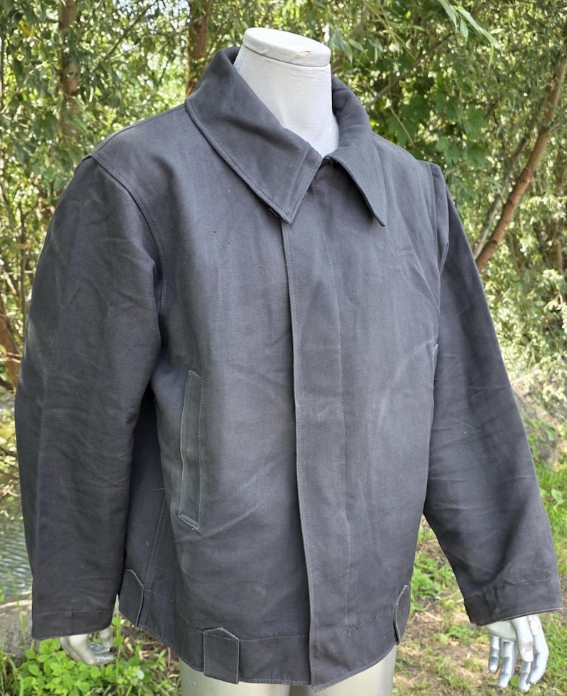 K&ouml;nnte beinhalten: Anthrazitfarbene Jacke mit breitem Kragen und zwei Vordertaschen. Die Jacke hat einen Knopfverschluss und einen geraden Saum. Die langen &Auml;rmel haben einfache Manschetten. Die Jacke ist aus robustem Material gefertigt.
