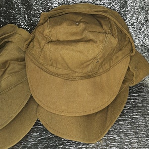May include: Two brown canvas military style caps with ear flaps. The caps are folded and stacked on top of each other.