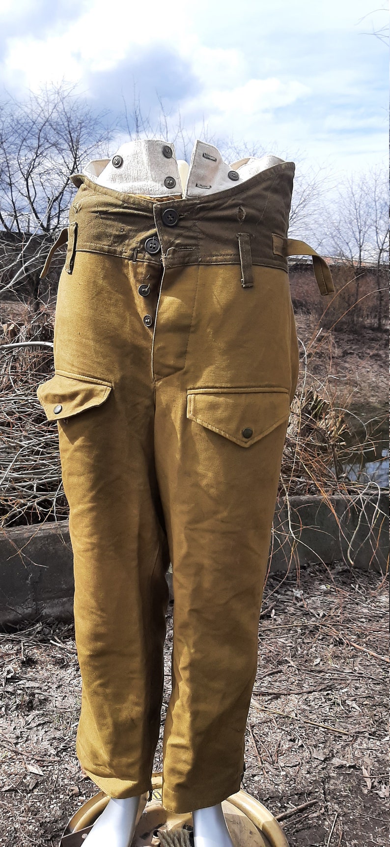 Op de afbeelding: Een broek van bruin canvas met een hoge taille en meerdere zakken. De broek heeft een knoopsluiting en een riemlus. De broek is gemaakt van een dik, duurzaam materiaal.