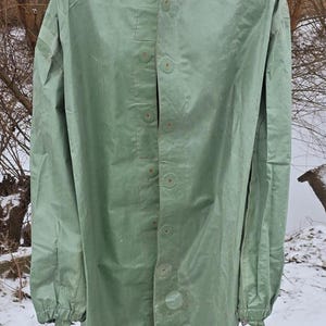 Op de afbeelding: Een groene regenjas met capuchon, knoopsluiting en lange mouwen. De regenjas is gemaakt van waterafstotend materiaal en heeft een capuchon met trekkoord.