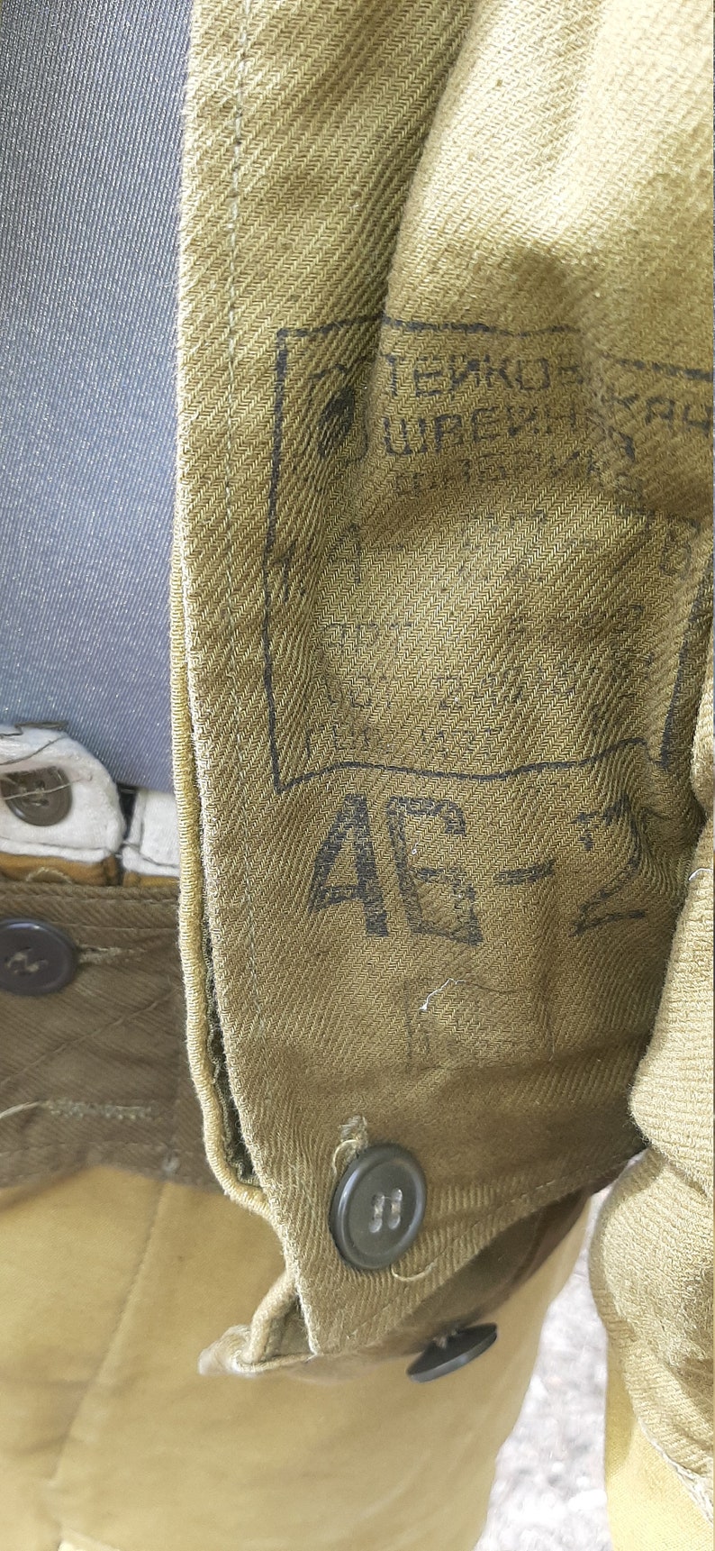 Op de afbeelding: Close-up van een bruin stoffen jack met een zwarte knoop en een label met de tekst "ТЕХНОЛОГИЯ УПРАВЛЕНИЯ".
