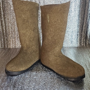 May include: A pair of brown felt boots with black rubber soles. The boots are tall and have a pointed toe.