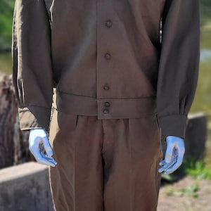 Peut inclure: Uniform de style militaire vert olive. La veste a deux poches de poitrine et des boutons. Le pantalon est de couleur et de style assortis. L'uniforme est présenté sur un mannequin.