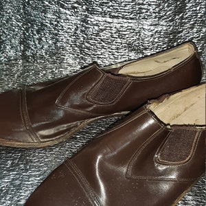 May include: A pair of brown leather slip-on shoes. The shoes have a cap toe design and elastic side panels. The leather has a glossy finish and shows signs of wear.