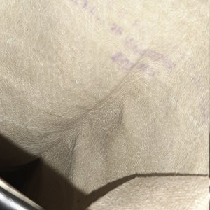 May include: The inside of a black leather boot with a white fabric lining. The lining has a textured surface and a purple inscription.