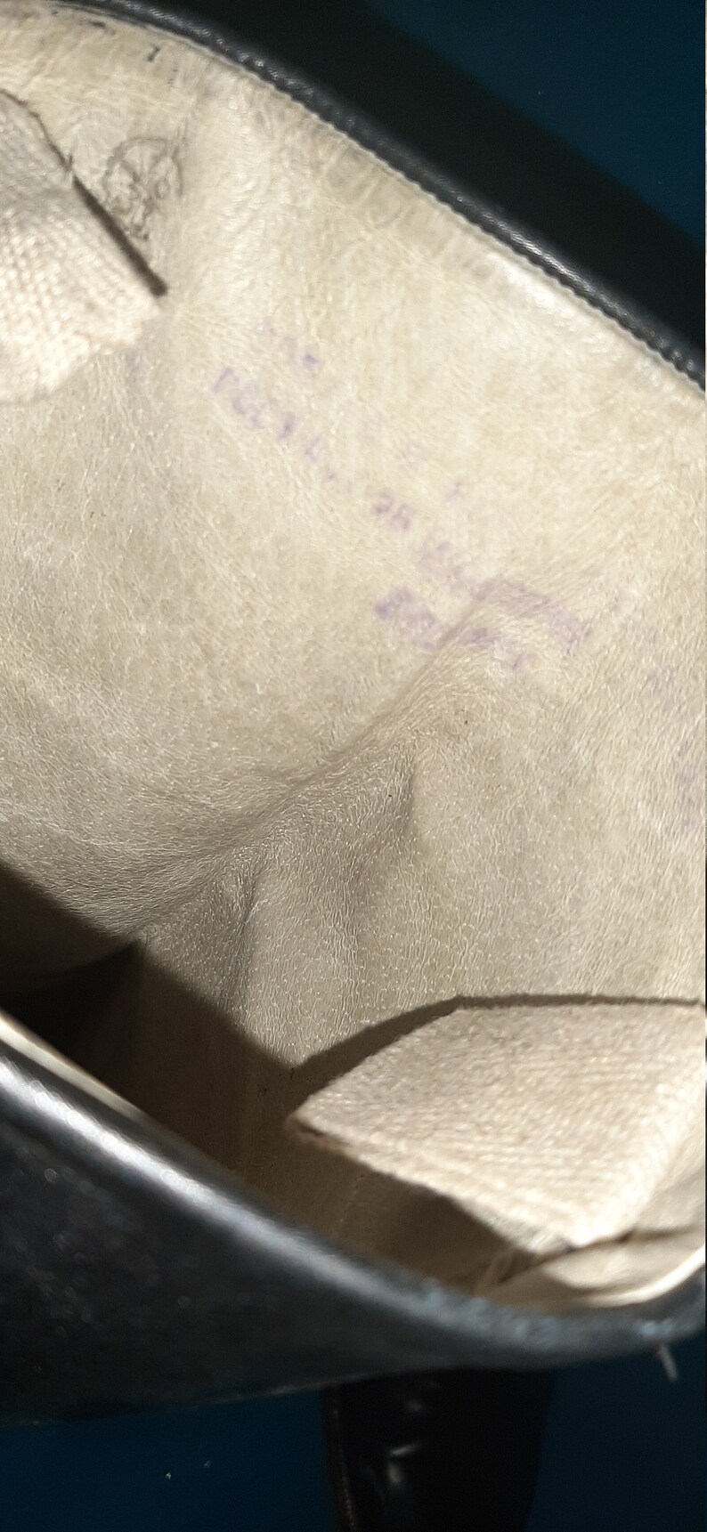May include: The inside of a black leather boot with a white fabric lining. The lining has a textured surface and a purple inscription.