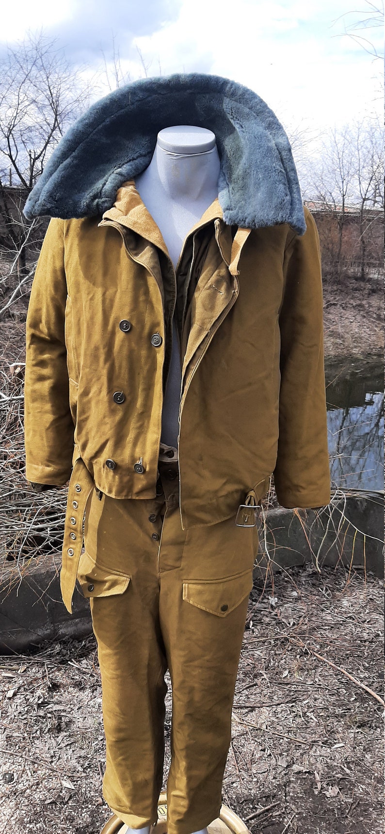 Op de afbeelding: Een bruin militair jack met een bontkraag en een bijpassende broek. Het jack heeft een dubbele rij knopen en een riem.