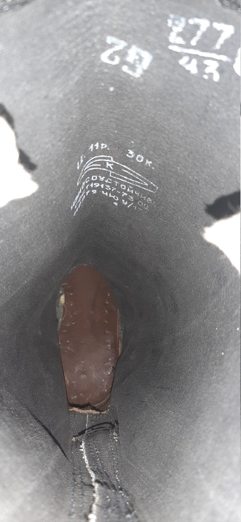 May include: Close-up of the inside of a black leather boot with white markings. The markings include the numbers 29, 43, 277, and 30K, as well as the letters "11P" and "R".