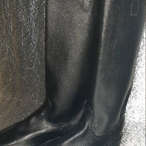 May include: A pair of black leather boots with a tall shaft and a rounded toe. The boots have a simple design and are made of a durable material.