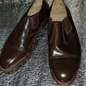 May include: A pair of brown leather slip-on shoes with elastic side panels. The shoes have a cap toe design and a low heel. The leather has a glossy finish, and the soles show signs of wear.