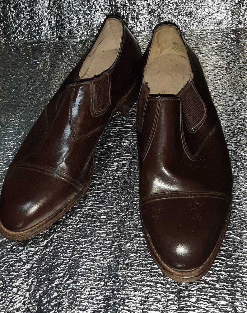 May include: A pair of brown leather slip-on shoes with elastic side panels. The shoes have a cap toe design and a low heel. The leather has a glossy finish, and the soles show signs of wear.