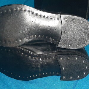 May include: A pair of black leather boots with a stitched sole and a row of metal studs around the edge.