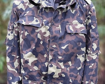 May include: A camouflage jacket with a black collar and a zipper closure. The jacket has multiple pockets and a button-up front.
