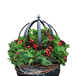May include: A black metal planter with a dome-shaped top, filled with green cedar branches and red berries.