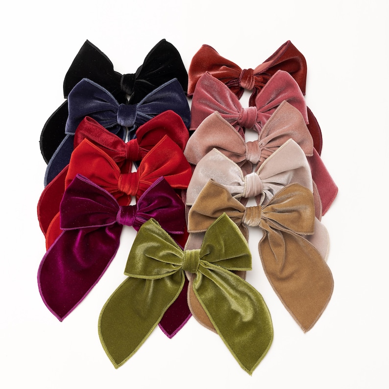 Puede incluir: Un conjunto de 10 lazos de pelo de terciopelo en varios colores, incluyendo rojo, rosa, verde, marr&oacute;n y negro. Los lazos est&aacute;n dispuestos en una pila, con el lazo m&aacute;s grande en la parte inferior y el lazo m&aacute;s peque&ntilde;o en la parte superior.