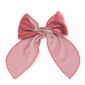 Puede incluir: Un gran lazo de terciopelo rosa con un clip plateado. El lazo est&aacute; atado en un estilo cl&aacute;sico con dos colas largas.