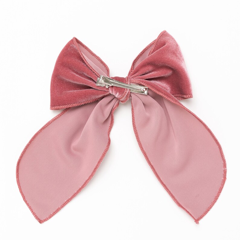 Puede incluir: Un gran lazo de terciopelo rosa con un clip plateado. El lazo est&aacute; atado en un estilo cl&aacute;sico con dos colas largas.
