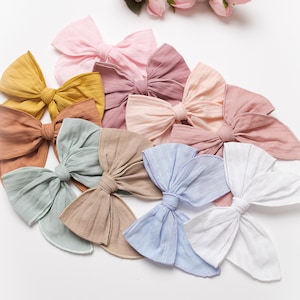 Op de afbeelding: Een set van tien haarstrikken van stof in verschillende kleuren, waaronder roze, blauw, wit, bruin en geel. De strikken zijn gemaakt van een zachte, gestructureerde stof en hebben een eenvoudig, elegant ontwerp.
