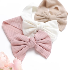May include: Three fabric headbands with large knotted bows. The headbands are in shades of pink, beige, and white.