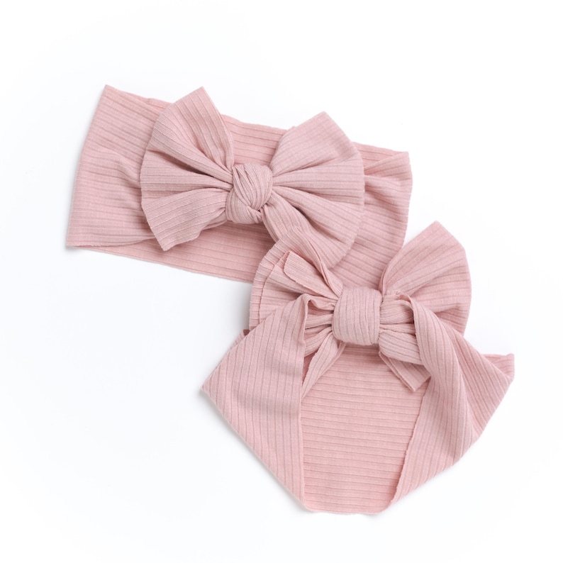 May include: Two pink ribbed fabric headbands with large bows. The headbands are made of a soft, stretchy material and are perfect for adding a touch of style to any outfit.