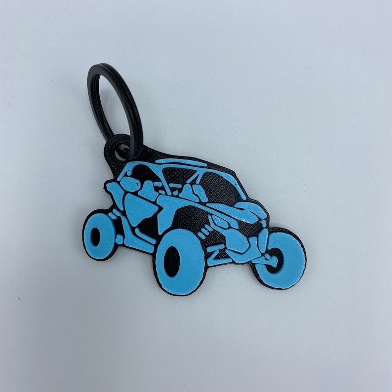 以下が含まれることがあります： 黒と水色のキーホルダーで、サイドバイサイドのオフロード車のシルエットが描かれています。