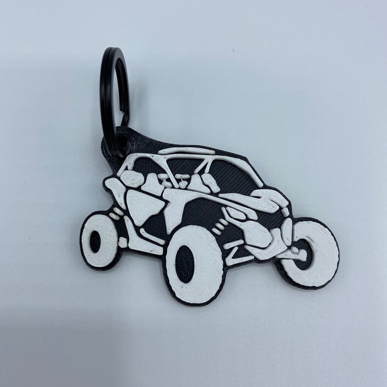 以下が含まれることがあります： 黒と白のキーホルダーで、白いオフロード車の横顔が描かれており、黒いリングが付いています。