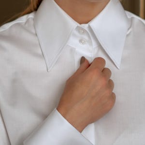 May include: A crisp white dress shirt with a classic collar and French cuffs. The cuff features a silver cufflink with a black center stone and surrounding clear stones. The shirt is buttoned at the collar.