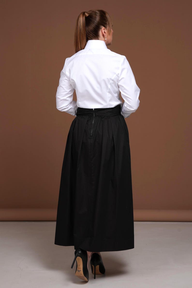 Back view of the white striped blouse from DaDonna Blouses, showcasing the impeccable fit and fabric quality. The shirt’s tailoring is crisp and feminine, crafted from premium 100% cotton. Styled with a dramatic black high-waisted skirt, this top is perfect for women who value refined elegance in their wardrobe. SEO-focused keywords: white cotton blouse, womens tops dressy, high collar blouse.