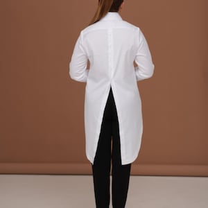 Back view of white shirt women with long tailcoat back and center back placket detail; crisp silhouette, high collar shirt shape, elegant womens dress shirt proportions.