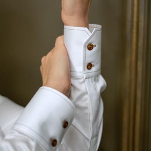 Detailed shot of the classic cuff with brown designer button and visible decorative stitching. The cuff design adds a timeless finish to the sleeve, suitable for pairing with a blazer or worn solo for a chic look.