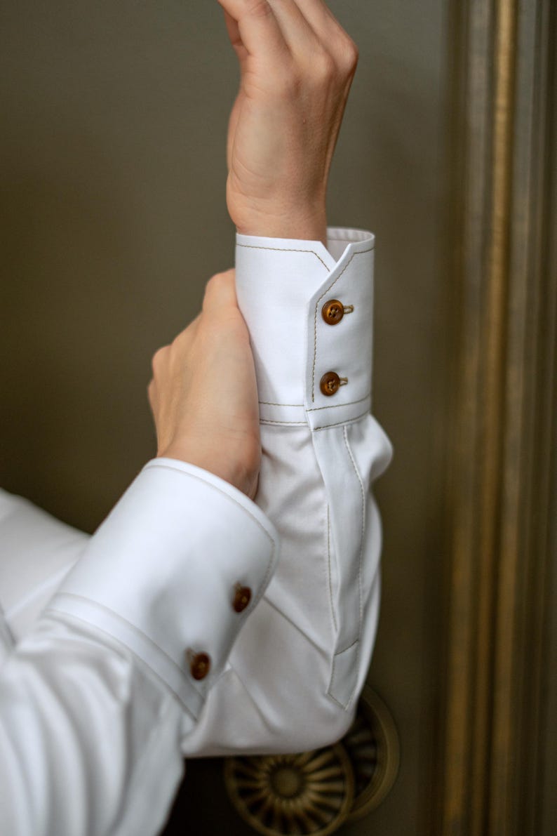Detailed shot of the classic cuff with brown designer button and visible decorative stitching. The cuff design adds a timeless finish to the sleeve, suitable for pairing with a blazer or worn solo for a chic look.