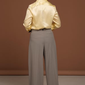 Back view of the butter yellow silk blouse showing the smooth, seamless construction and graceful fit across the shoulders and back. The glossy finish of the silk highlights the garment’s luxurious texture and refined tailoring, demonstrating the superior cut and quality of this exclusive piece