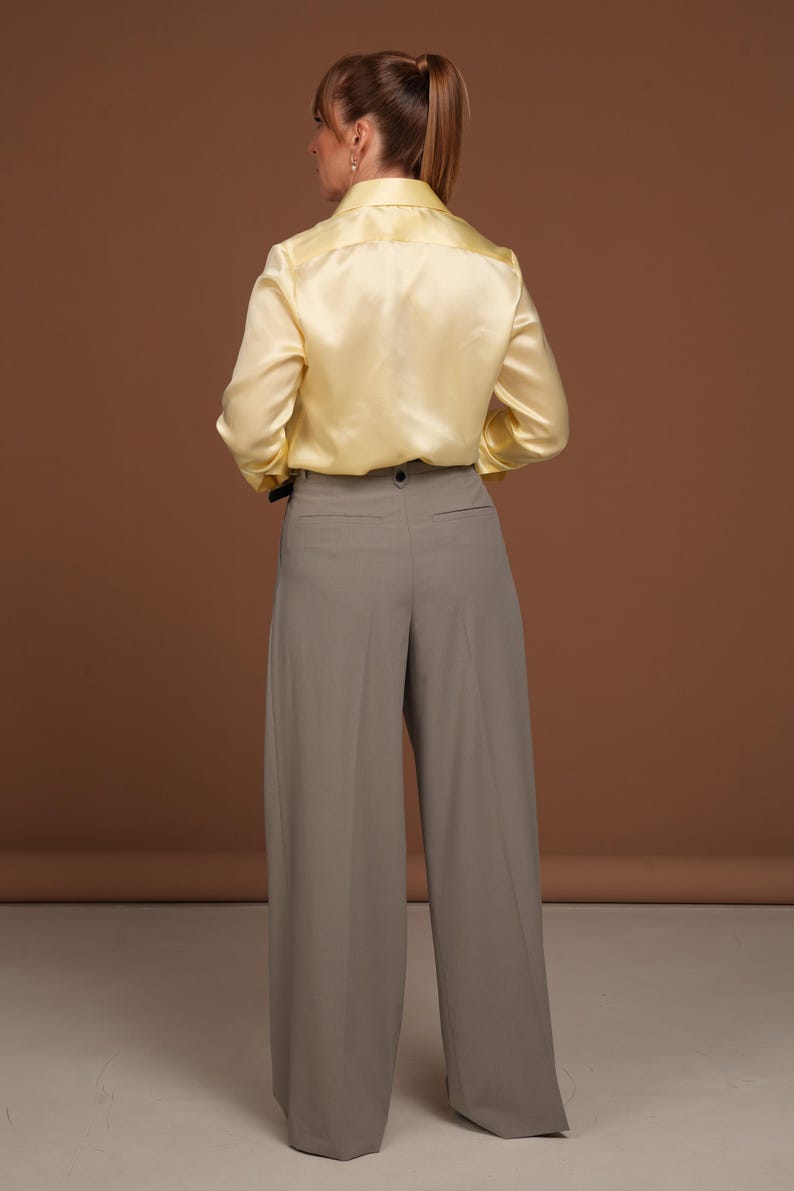 Back view of the butter yellow silk blouse showing the smooth, seamless construction and graceful fit across the shoulders and back. The glossy finish of the silk highlights the garment’s luxurious texture and refined tailoring, demonstrating the superior cut and quality of this exclusive piece