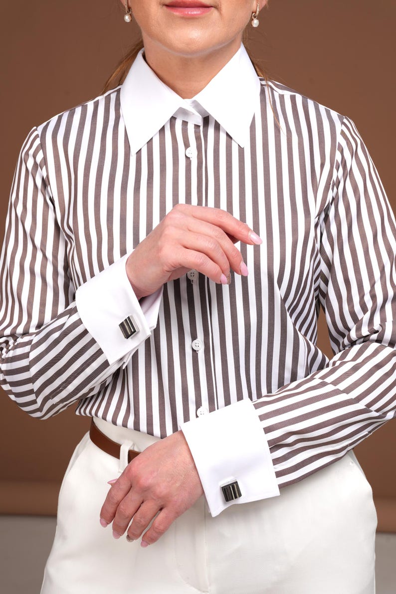 Wrist-level close-up of the French cuffs adorned with sleek metal cuff links. The craftsmanship highlights precision, with clean white double cuffs framing the striped fabric beautifully. This high-end women’s dress shirt is designed for those who appreciate elite business fashion, exceptional fabric, and professional attire that stands out. Custom-made for luxury wear.