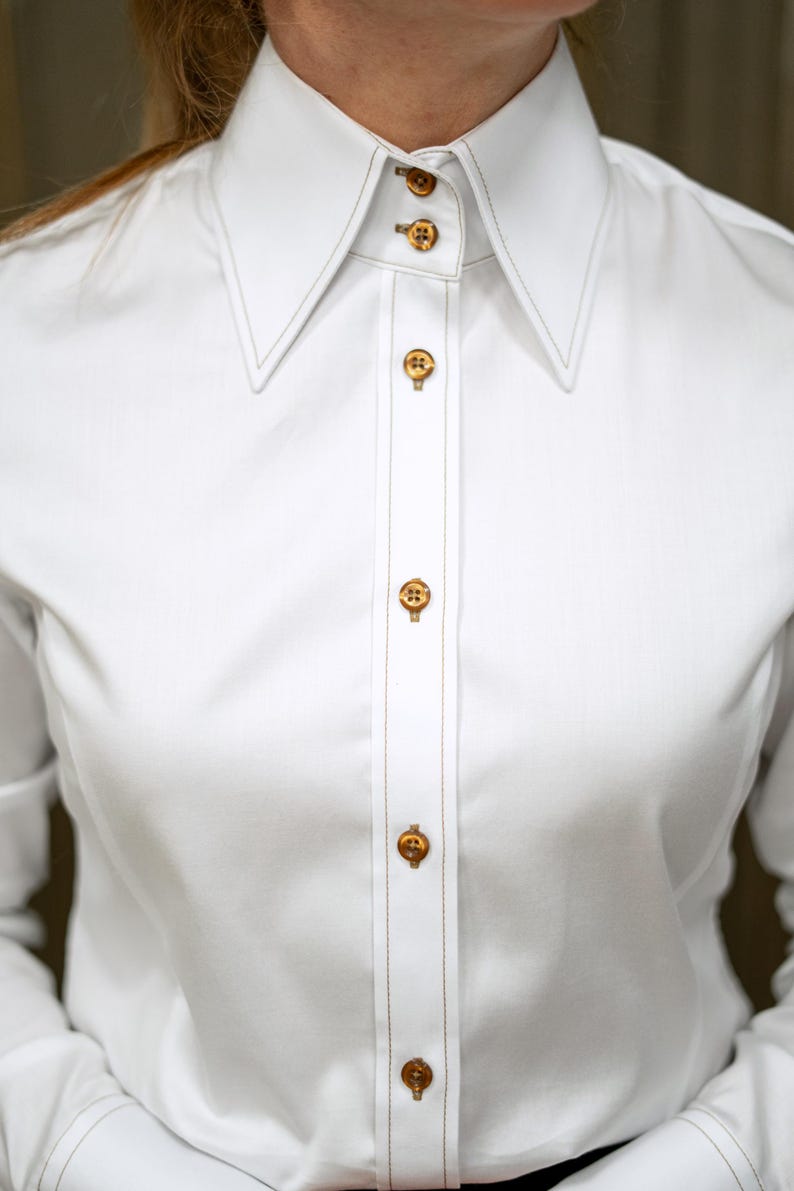 Zoomed-in view of the high collar structure, revealing expert tailoring and firm construction. The brown topstitching along the edge adds a modern contrast to the pristine white fabric, showcasing luxurious craftsmanship.