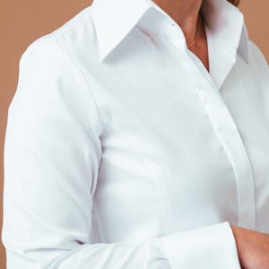 K&ouml;nnte beinhalten: Ein wei&szlig;es Langarmhemd mit einem strukturierten Kragen und Umschlagmanschetten, die mit silberfarbenen, dekorativen Manschettenkn&ouml;pfen befestigt sind. Das Hemd verf&uuml;gt &uuml;ber eine glatte Knopfleiste und einen schlichten, ebenm&auml;&szlig;igen Stoff.