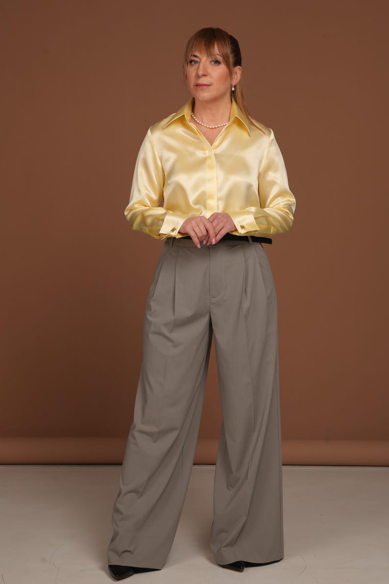 Front-facing image with high collar buttoned to the top, highlighting the structured elegance and modern femininity of the silk blouse. Paired with tailored trousers, this refined look speaks to confident, stylish women who value comfort and quality in formalwear