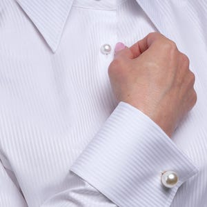 Close-up portrait showing the elegant white blouse with high standing collar and luxury pearl buttons. The crisp cotton fabric has a delicate striped texture, making it ideal for women seeking a sophisticated and timeless business or evening look. Styled with drop pearl earrings for an extra touch of class. Keywords: white top, white formal blouse, French cuff blouse