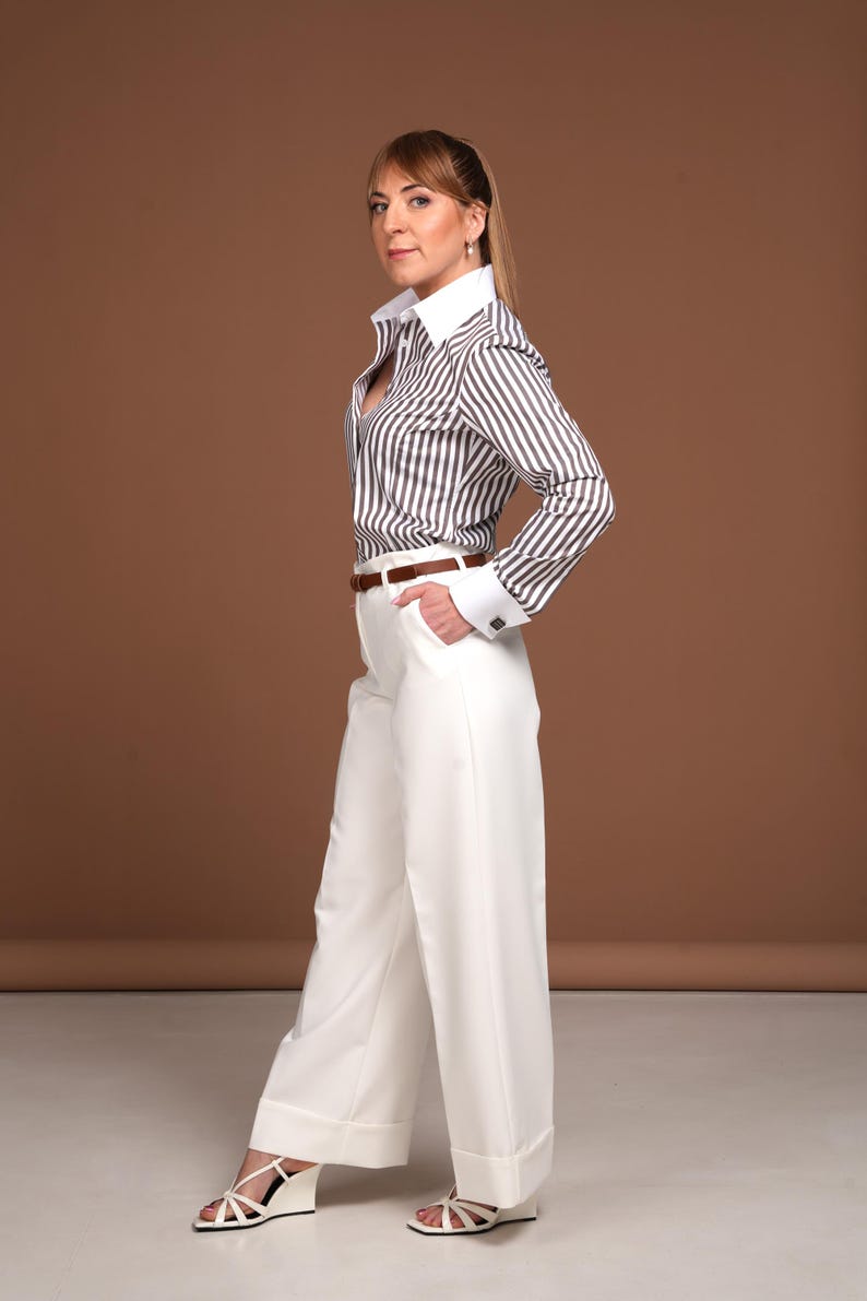 Side view of a woman wearing a luxury brown striped women's French cuff shirt with white collar and double cuffs. This elegant button down business shirt is crafted from premium cotton and tailored to perfection. Perfect for formal wear, office fashion, or upscale casual styling. A sophisticated and timeless dress shirt for women who appreciate exclusive quality and a powerful wardrobe statement.