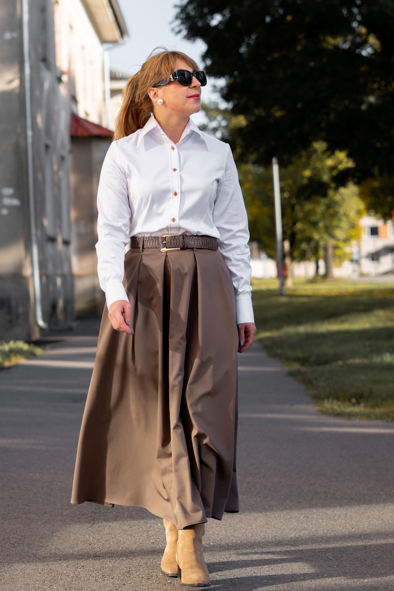 Flat lay of the white blouse, highlighting button and stitching details from a top-down view. This image also confirms that the shirt comes with brown designer buttons and decorative contrast stitching. Accessories pictured are for styling only and not included.