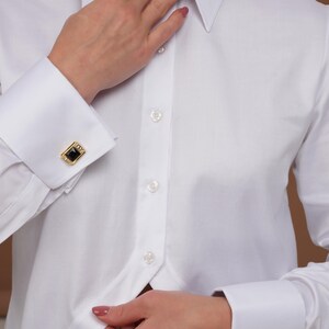 Three-quarter portrait in a white tuxedo blouse, statement collar and clean lines; French cuffs visible as a cufflink shirt women can style for evenings (cufflinks not included).
