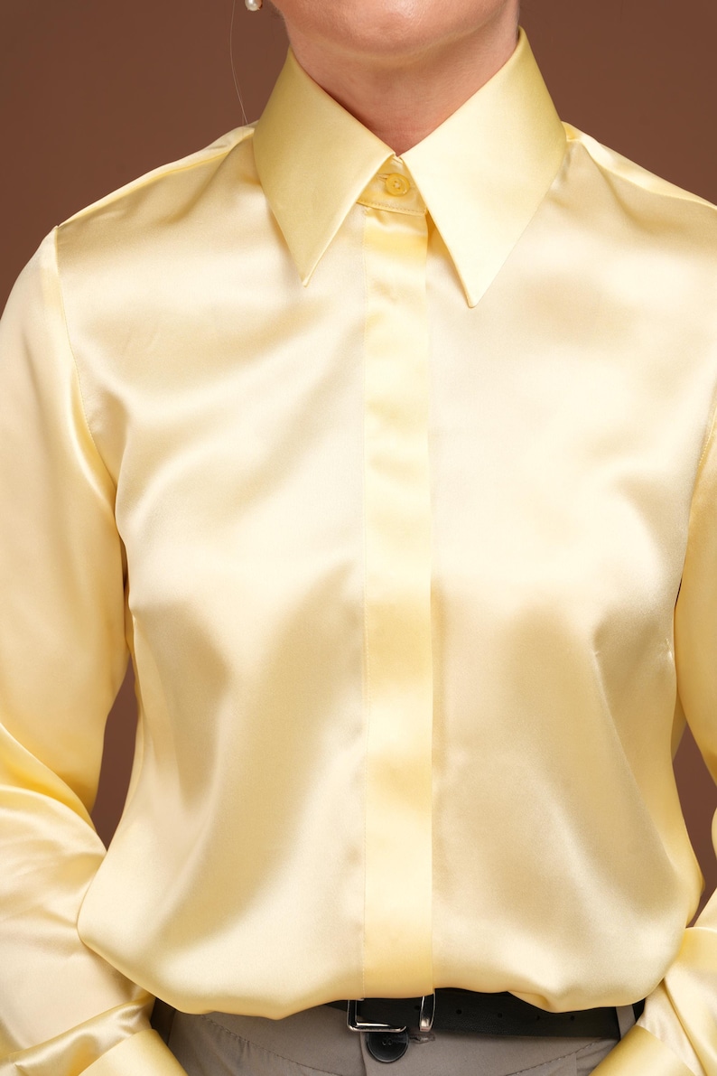 Close-up of the chest area, capturing the natural glow of the silk material and the precise stitching around the collar and button placket. The smooth finish of the luxurious fabric showcases the blouse as a standout piece in any wardrobe