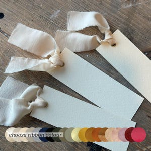 May include: Cream-coloured rectangular tags with off-white ribbon ties. The tags have a textured surface and a small hole for the ribbon. A colour palette with the text "choose ribbon colour" is also visible in the image.