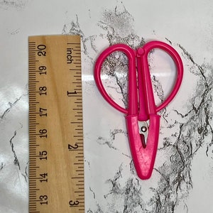 May include: Pink heart-shaped scissors with silver blades. The scissors are approximately 12.5 cm long.
