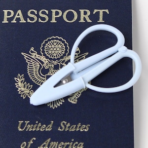 Peut inclure: Ciseaux de voyage bleu clair posés sur un passeport américain bleu marine. Le passeport porte des lettres dorées et un emblème doré. Les ciseaux ont une poignée en boucle et une lame argentée.