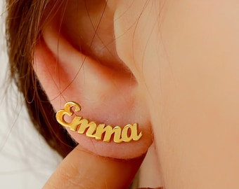May include: Gold-toned nameplate earrings with the name "Emma" spelled out in a cursive font.