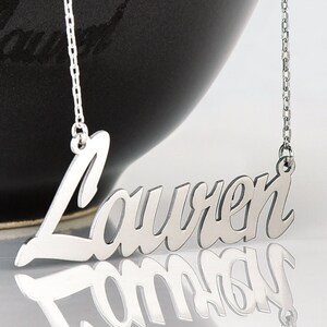 May include: A silver necklace with a cursive nameplate pendant that reads "Lauren".
