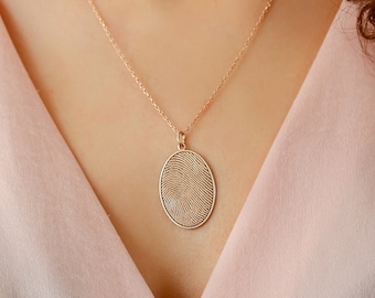 May include: A gold chain necklace with a delicate oval pendant featuring a textured design. The necklace is worn by a person with long brown hair.