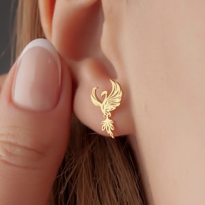 May include: Gold phoenix earrings with intricate details. The earrings are small and delicate, perfect for everyday wear.
