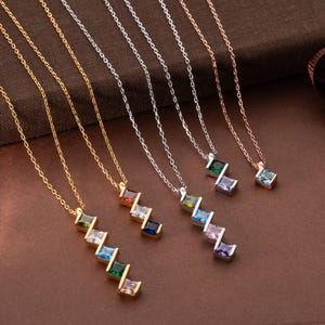 Puede incluir: Una colección de collares con cadenas de oro, plata y oro rosa. Cada collar presenta una serie de piedras preciosas de corte cuadrado en varios colores, incluyendo verde, azul, morado y transparente. Las piedras están dispuestas en un patrón en zigzag.
